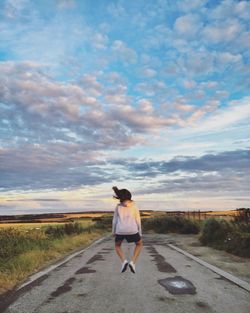 Rear view of woman jumping over road against sky