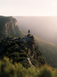 Rear view of woman standing on cliff against sky