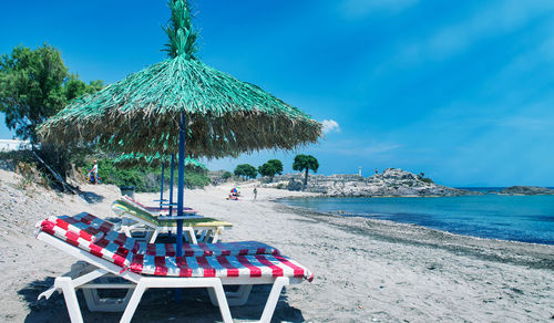 Lounge chairs and parasols on beach against sky