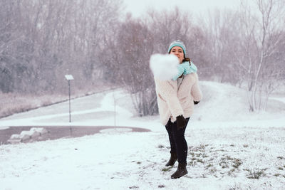 Portrait of young woman playing with snow at park during winter