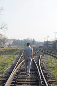 Rear view of man walking on railroad tracks against clear sky