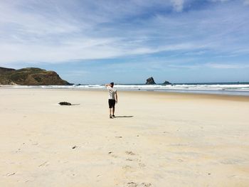 Rear view of woman standing on beach against sky