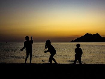 Silhouette people on beach against sky during sunset