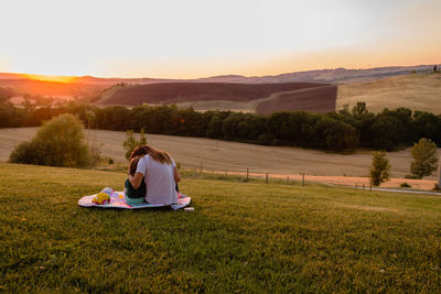 Mother and daughter sitting on field against sky during sunset