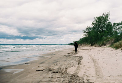 Rear view of woman walking at beach against sky