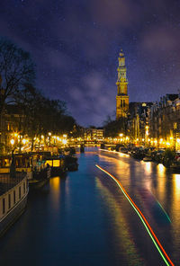 Illuminated buildings by river against sky in city at night