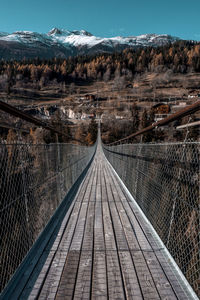 Empty footbridge against snowcapped mountain