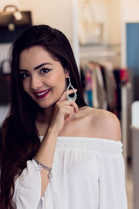 Portrait of smiling young woman trying earring while standing in store