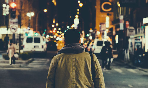 Rear view of man walking on illuminated street amidst buildings