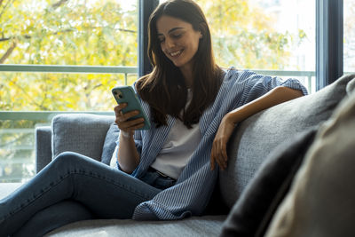 Young woman using phone while sitting on sofa at home