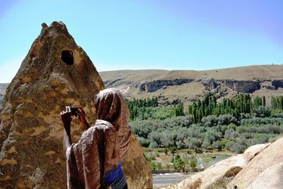 Rear view of woman photographing by mountain against clear sky