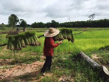 Side view of woman working on field against cloudy sky