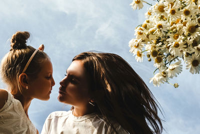 Low angle view of mother kissing daughter by flowers against sky