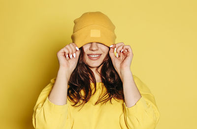 Portrait of smiling young woman against yellow wall