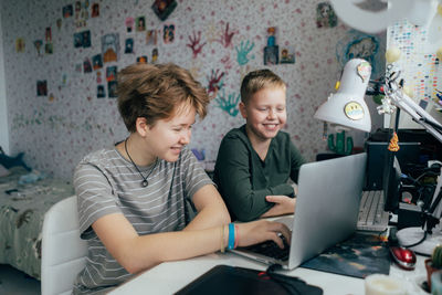 Laughing cheerful brother and sister are watching entertainment video content on a laptop.