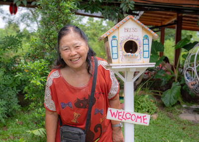 Portrait of smiling woman standing by birdhouse against plants