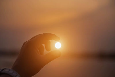 Close-up of hand holding sun during sunset