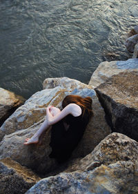 High angle view of woman in fetal position on rock by sea