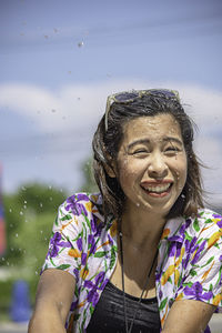 Smiling woman splashing water against sky