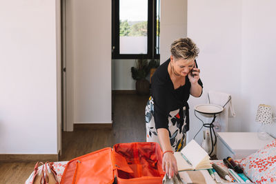 Side view of young woman using mobile phone while sitting on bed at home