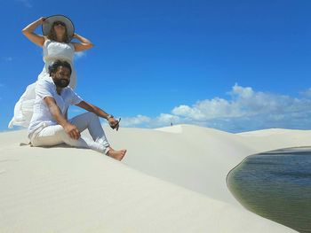 Smiling couple at sandy beach against blue sky