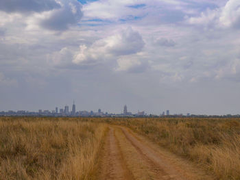 Dirt road amidst field against sky
