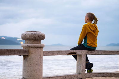 Lonely teenager looking to sea sitting on the waterfront. rear view of teenager against seascape.