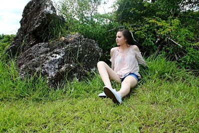 Low angle view of young woman sitting on grassy field