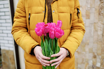 Blond man in a yellow winter jacket with a bouquet of tulips in hands