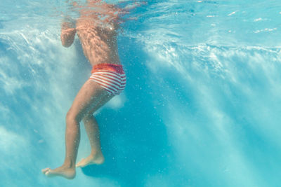 Underwater view of cropped unrecognizable kid swimming in clear water of pool and looking at camera