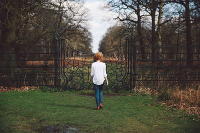 Rear view of young woman on grassy field walking towards closed gate