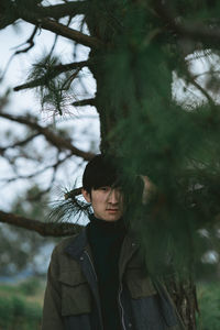 Portrait of man seen through leaves standing against tree trunk