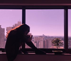 Sad woman sitting on window sill 