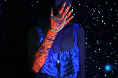 Midsection of woman standing against illuminated lights at night