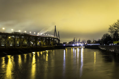River by illuminated bridge against sky at dusk