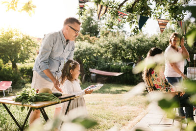 Grandfather with granddaughter carrying food in plate at backyard