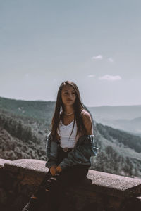 Girl looking away while sitting against sky