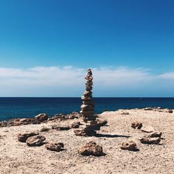 Stones stacked on cliff by sea against sky