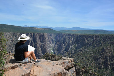 Full length of woman sitting on rock against sky