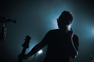 Low angle view of silhouette man against illuminated light at night