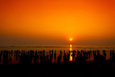 Silhouette people on beach against sky during sunset