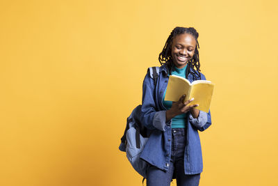 Portrait of young woman standing against yellow background