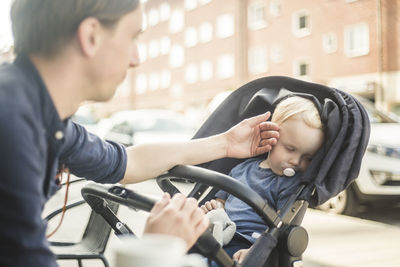 Father looking at baby sleeping on stroller in city