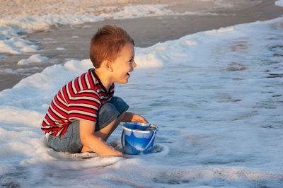 Side view of cute happy boy playing on shore at beach during sunset