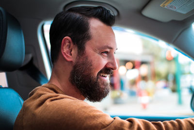 Side view of smiling bearded man sitting in car