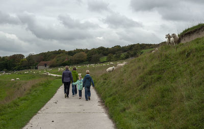 Rear view of people walking on landscape against sky