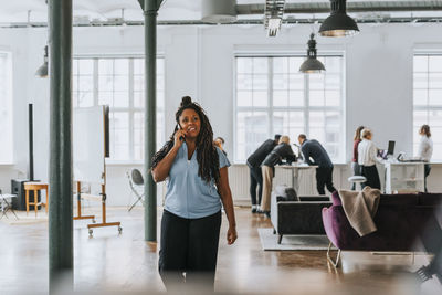 Thoughtful businesswoman talking on smart phone while walking in office