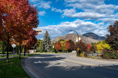 Road by trees against sky during autumn