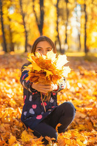 Portrait of woman holding autumn leaves during sunset