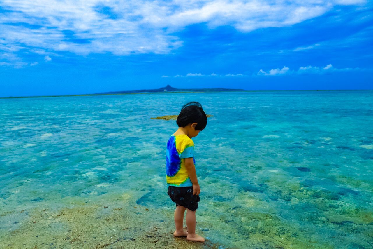 sea, water, sky, horizon over water, child, real people, scenics - nature, horizon, one person, blue, beauty in nature, leisure activity, cloud - sky, childhood, lifestyles, land, nature, day, standing, outdoors, turquoise colored, shorts